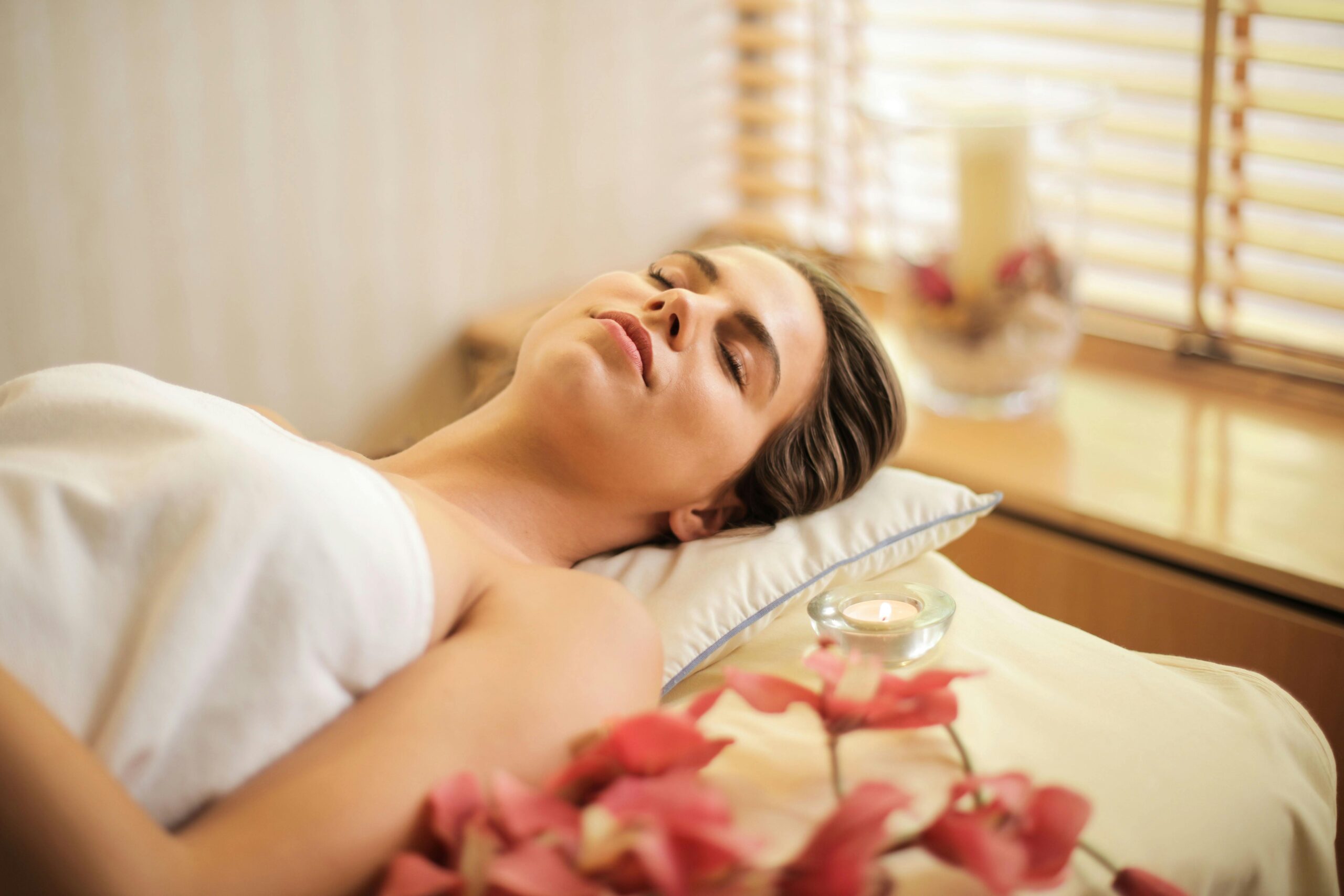 Woman enjoying a relaxing spa day with flowers and candles indoors.